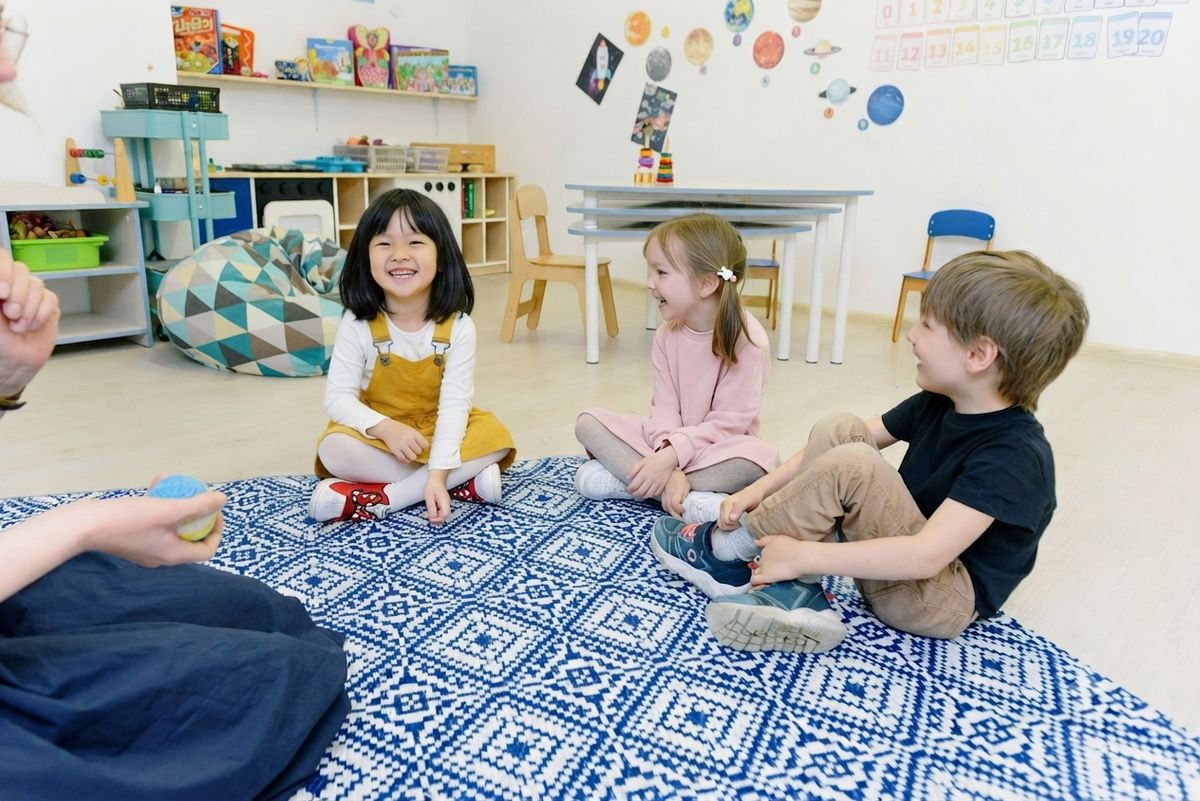 Children sitting together on a rug in a classroom, smiling and interacting