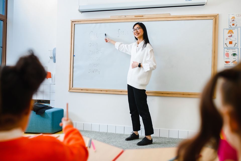 A teacher writing on a whiteboard at the front of a classroom while students watch