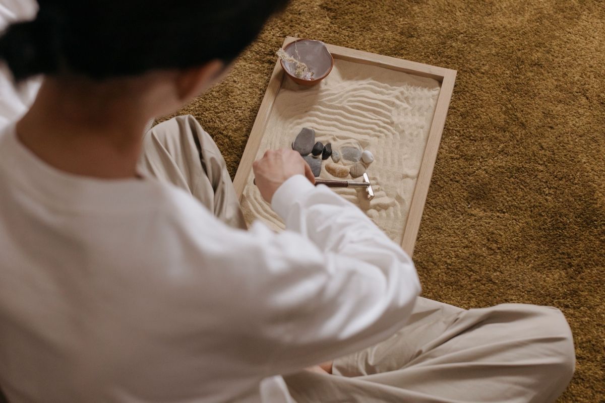 A child sitting on a carpet, arranging stones and raking patterns in a small sand tray