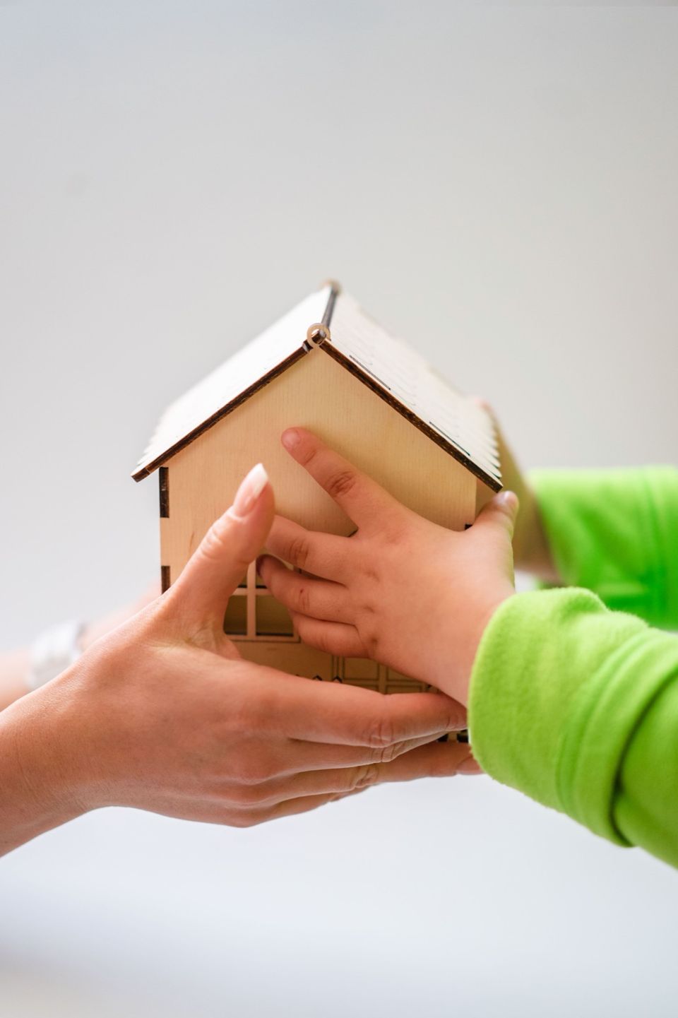 An adult's hand and a child's hand holding a small wooden toy house together