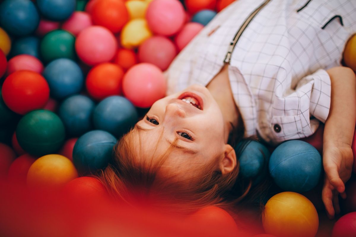 A child lying in a colorful ball pit, laughing
