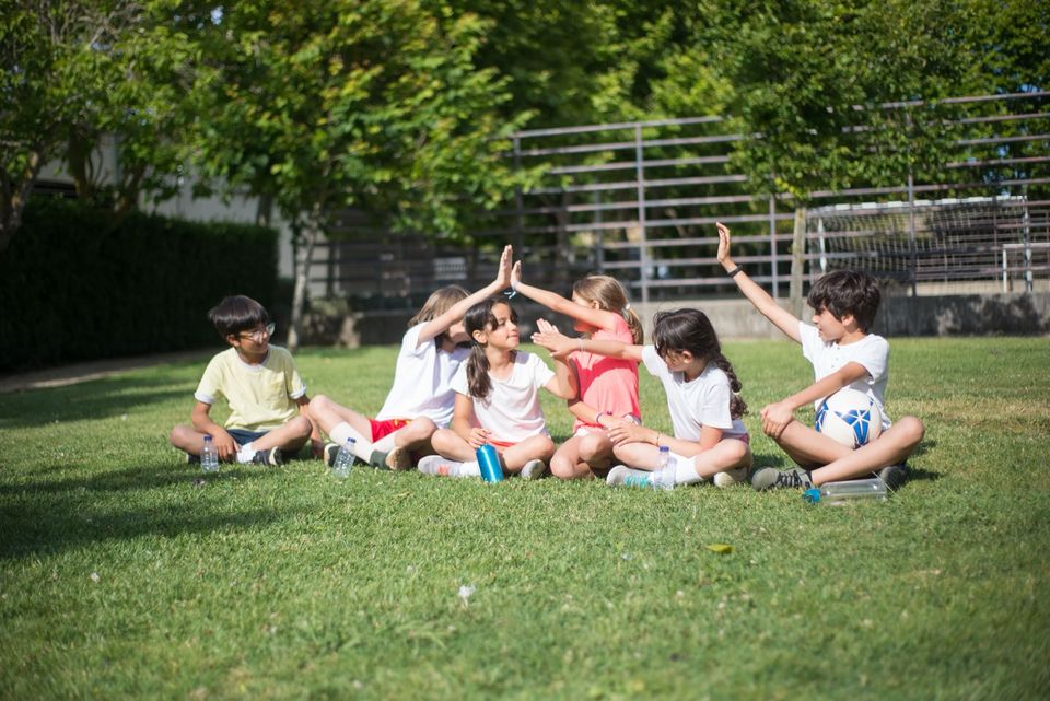 Children sitting on the grass, giving each other high-fives