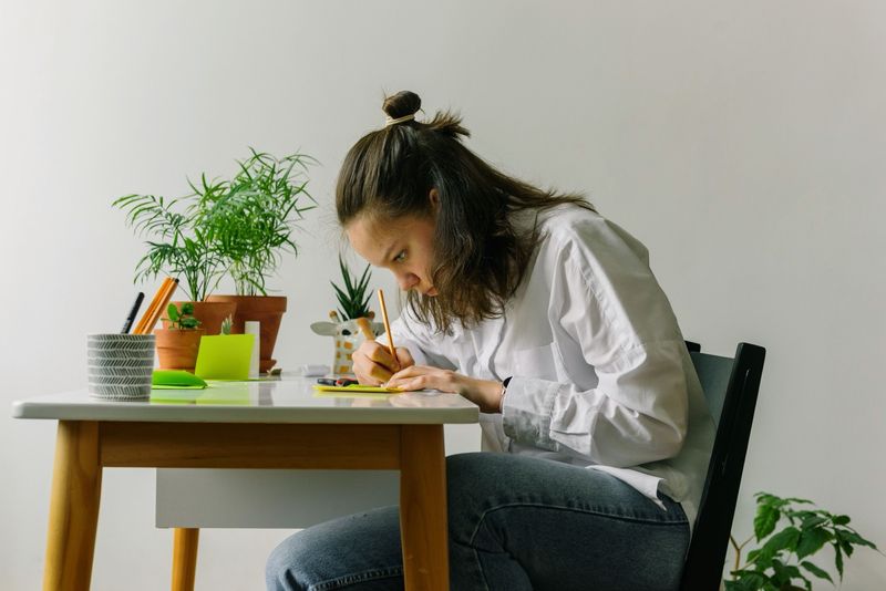 一个女孩在书桌前专注书写，旁边摆放着绿植和便利贴