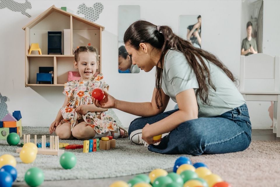 A counselor and a young girl playing with toys together on a rug