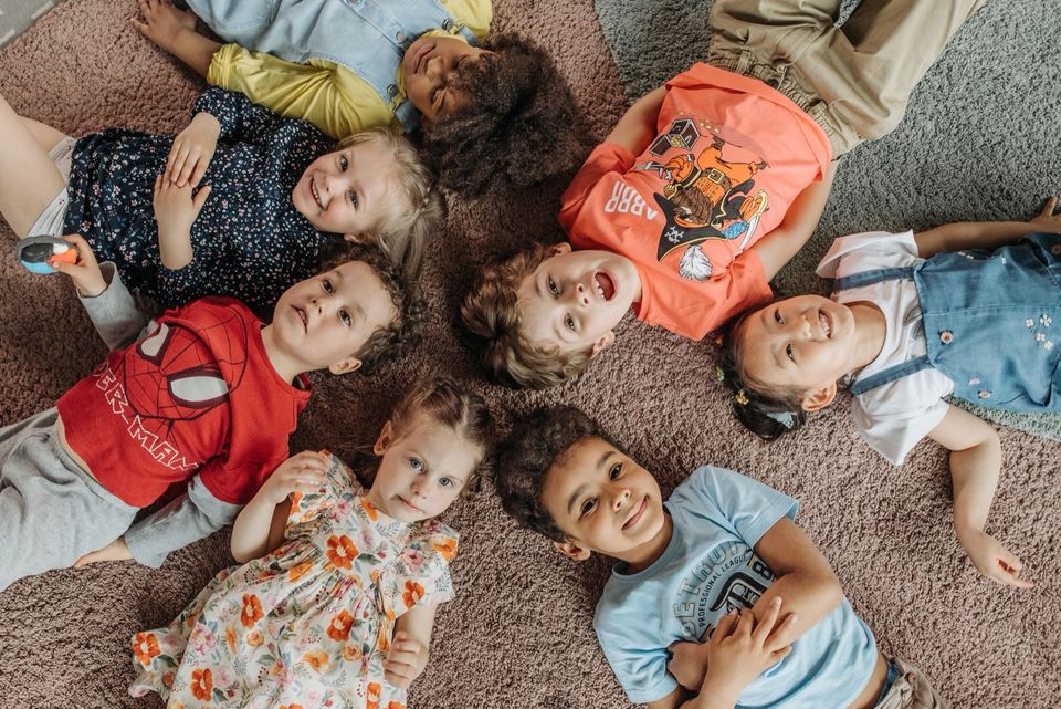 Young children lying in a circle on a carpet, smiling up at the camera