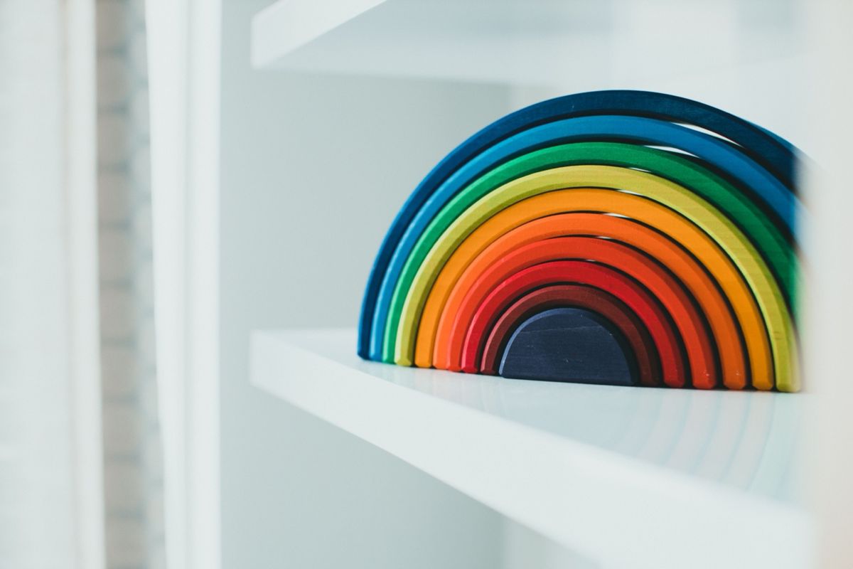 A colorful wooden rainbow stacking toy resting on a white shelf